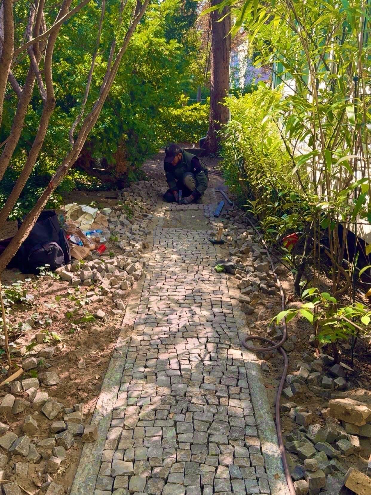 Verlegung eines Natursteinpflasters in enger Gartenumgebung.